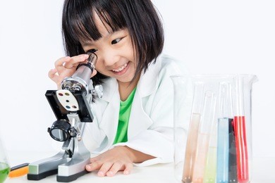 smiling asian chinese little girl working with microscope in isolated white background.