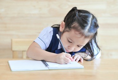 little asian school girl writing notebook homework with pencil on the table