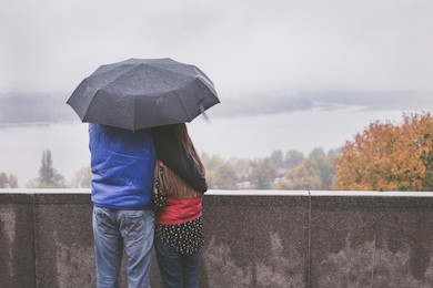 romantic happy couple hugging in the street standing under an umbrella in the rain
