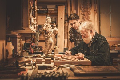 senior restorer and his apprentice working with antique decor element in his workshop.