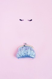 a shiny silver female purse and eyelashes on light pink background