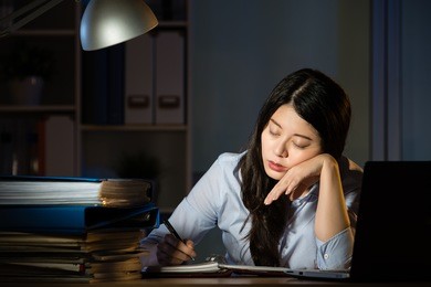 asian business woman sitting at desk sleepy working overtime late night. indoors office background