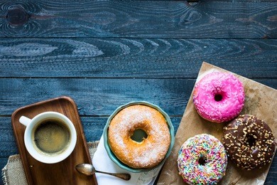 colorful donuts and coffee breakfast composition with different color styles of doughnuts over an aged wooden desk background.