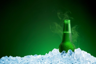 bottle of cold beer in ice on green background