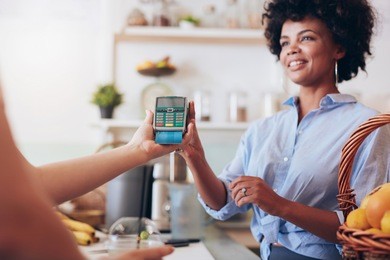 cropped shot of a female customer paying for her juice by credit card at juice bar. focus on woman hands holding credit card reader.