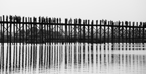 black and white photo of old wooden bridge and many people on it , u bein bridge is a crossing that spans the taungthaman lake near amarapura, myanmar