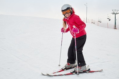 smiling teenage girl equipped for skiing on snowy slope at ski resort.