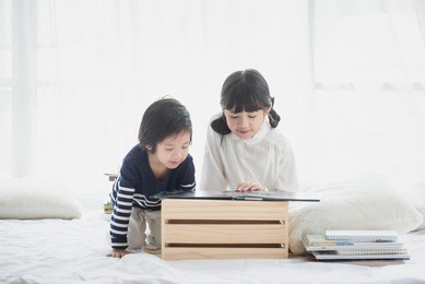 cute asian children reading a book on white bed