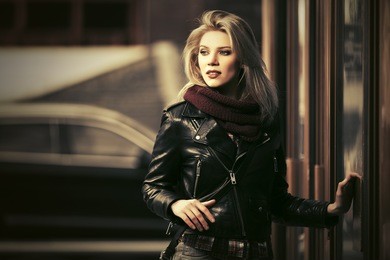 young fashion blond woman next to mall door on city street stylish model in black leather jacket and snood scarf 