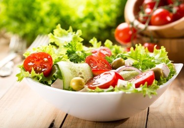 bowl of salad with vegetables and greens on wooden table