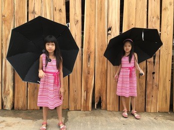 twin girl in a pink dress with black long hair with an umbrella little girl holding  umbrella happy asian girl outdoor. girl with an umbrella girl umbrella stand in the hot sun with wood background