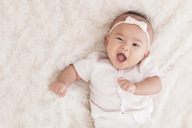 close up portrait of adorable baby girl with funny expression lying on fur blanket with copy space