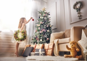 merry christmas and happy holidays!  cute little child girl is decorating the christmas tree indoors.