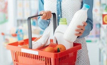 woman shopping at the supermarket, she is carrying a shopping basket and taking a milk bottle