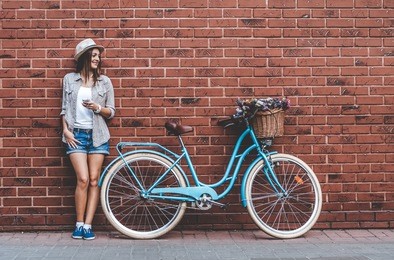 beauty with vintage bike. beautiful young smiling woman standing near her vintage bicycle with basket full of flowers while she leans against the wall.