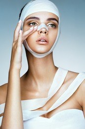 woman removes the bandages from her head and touching her new face. portrait of young models face in medical bandage after beauty surgery. plastic surgery concept