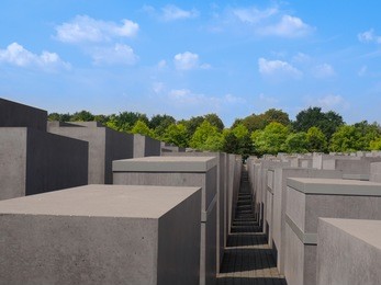 the memorial to the murdered jews of europe in berlin with green tries and blue sky in the background