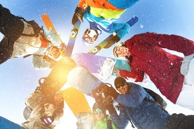 group of happy skiers and snowboarders stands in circle and smiling
