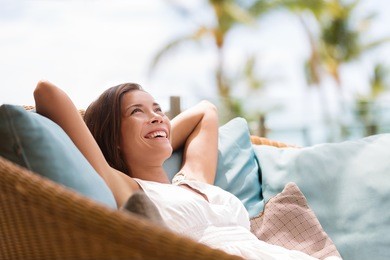 home lifestyle woman relaxing enjoying luxury sofa patio furniture on outdoor patio living room. happy lady lying down on comfortable pillows daydreaming thinking. beautiful young asian chinese girl.