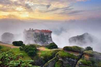 meteora monasteries. beautiful view on the holy monastery of varlaam placed on the edge of high rock covered of the morning clouds and mist at sunrise, kastraki, greece