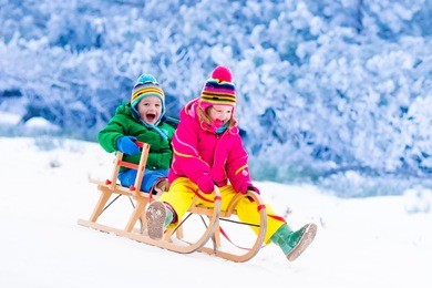 little girl and boy enjoy a sleigh ride. child sledding. toddler kid riding a sledge. children play outdoors in snow. kids sled in alps mountains in winter. outdoor fun for family christmas vacation.