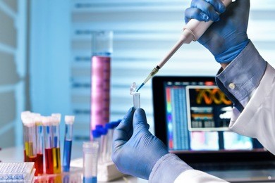 scientist holding tube and working with laptop at genetic lab / hands of engineer genetic working in laboratory