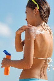 sunscreen bikini woman putting lotion on shoulder and back on beach vacation in summer holidays. girl applying sun skincare solar protection cream product on body holding bottle sunbathing.
