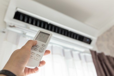 air conditioner inside the room with woman operating remote controller. / air conditioner with remote controller
