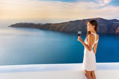 luxury hotel terrace. europe destination summer vacation. asian woman drinking red wine relaxing enjoying view of the mediterranean sea in oia, santorini, greece. honeymoon high end travel holiday.