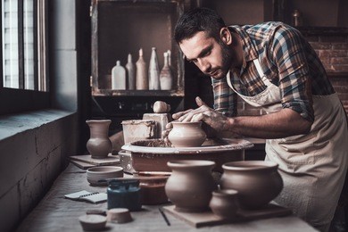 total concentration at work. confident young man making ceramic pot on the pottery wheel