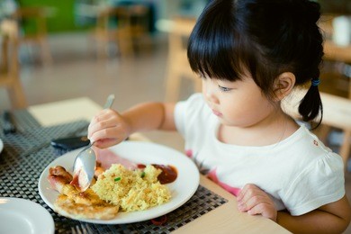 happy little asian girl eat yellow rice on breakfast time.