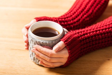 hot mug of tea warming woman's hands in retro woollen jumper. wooden table