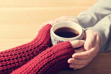 a couple in love warming hands with a hot mug of tea. wearing cosy woollen jumpers.
