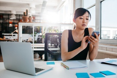 portrait of young asian woman sitting at her desk with laptop and adhesive notes using mobile phone. asian businesswoman working in modern office.