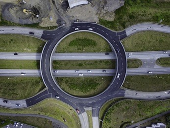 aerial image of a roundabout over a 4 lane highway, cars on the road and road construction to the side