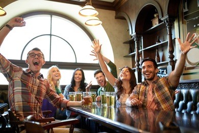 people, leisure, friendship and entertainment concept - happy friends drinking beer, watching sport game or football match and celebrating victory at bar or pub