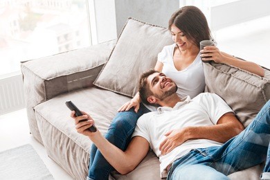 cheerful beautiful young couple drinking coffee and watching tv at home