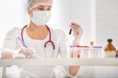 serious female scientist is analyzing blood sample in laboratory. she is sitting and writing