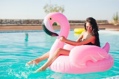 girl sits on inflatable mattress flamingos in the pool