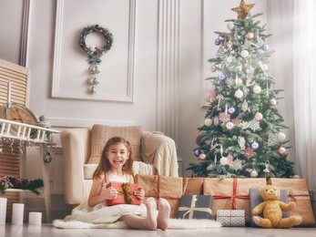 merry christmas and happy holidays! cheerful cute little child girl with present. kid holds a gift box near christmas tree indoors.