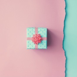 close up shot of small gift wrapped with pink ribbon on pink blue background. christmas background. minimal concept. flat lay. top view.