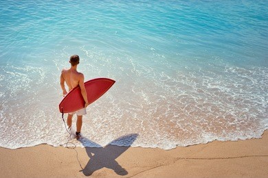 it's time for surfing! young man holding surf board on the sea shore.