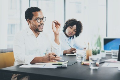 black african project manager explaning business task in meeting room.two young entrepreneurs working together in a modern office.horizontal,blurred background