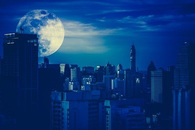 silhouettes of skyscrapers different construction in the dark town with background of a large moon and clouds at nighttime. dark tone. the moon were not furnished by nasa.