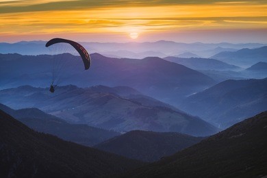 paraglide silhouette in a light of sunrise above the misty carpathian mountain valley. 