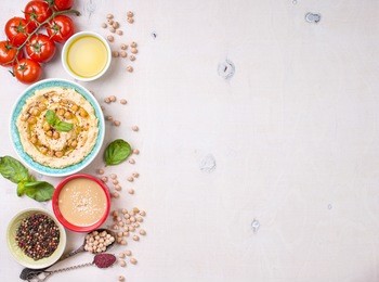 bowl with hummus, chickpea, tahini, olive oil, sesame seeds, cherry tomatoes and herbs on white rustic wooden background. space for text/food frame. middle eastern cuisine. top view. hummus background