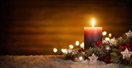 burning candle and christmas decoration over snow and wooden background, elegant low-key shot with festive mood