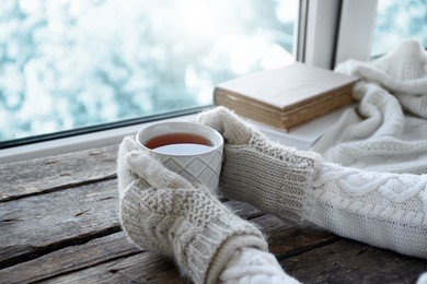 female hands holding hot drink on windowsill