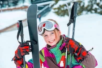 happy kid holding skis and ski poles  in hands, sitting in snow