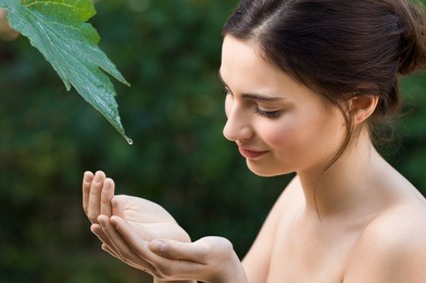 beautiful young woman take a drop of clear water from a leaf in the nature. natural beauty refresh herself with water directly from a vine leaf. symbol of purity, body care and nature harmony.